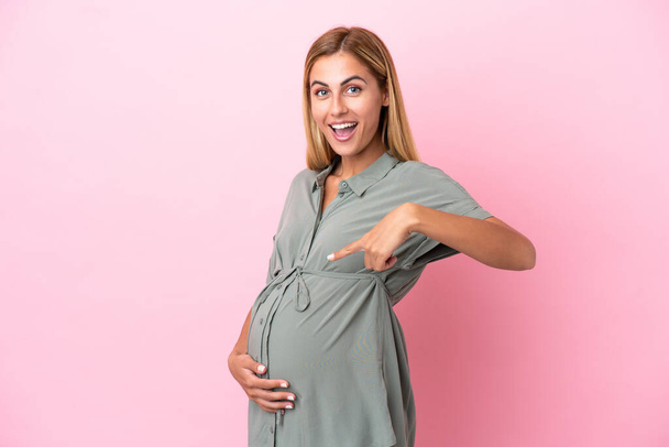 Young Uruguayan woman isolated on blue background pregnant and pointing to the belly - Foto, Bild