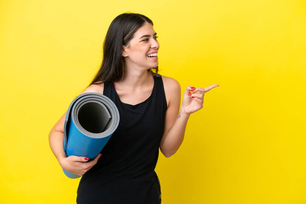 sport Italian woman going to yoga classes isolated on yellow background pointing finger to the side and presenting a product - Photo, Image