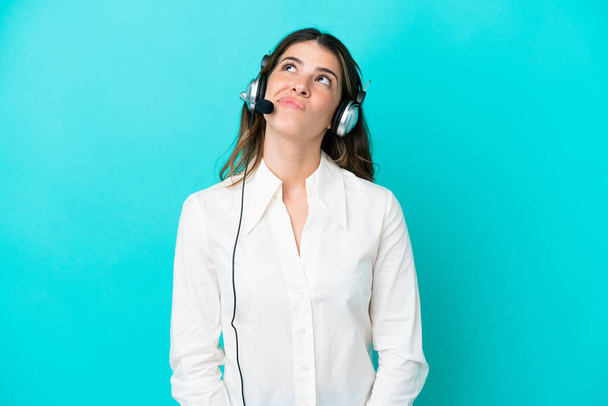 Telemarketer olasz nő dolgozik egy headset elszigetelt kék háttér és felnéz - Fotó, kép