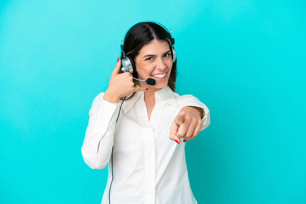 Італійська жінка, що працює з навушником на синьому фоні, робить жест телефона і вказує спереду. - Фото, зображення