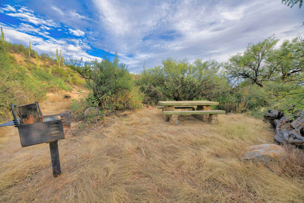 Em churrasqueira de madeira moída perto de uma mesa de piquenique em um acampamento no Parque Estadual Sabino Canyon em Tucson, AZ. Há um poste de grade à esquerda perto da mesa de concreto e cadeiras contra o deserto. - Foto, Imagem
