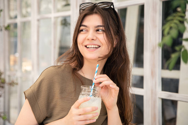 Ελκυστική νεαρή γυναίκα με ένα ποτήρι δροσιστική λεμονάδα σε μια ζεστή καλοκαιρινή μέρα. - Φωτογραφία, εικόνα