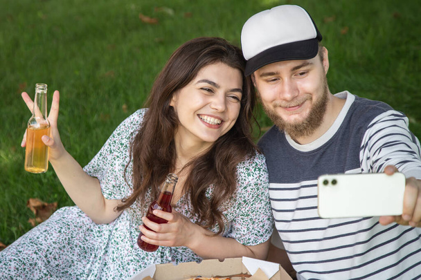 A young man and woman take a selfie with pizza at a picnic, outdoor recreation. - Фото, изображение