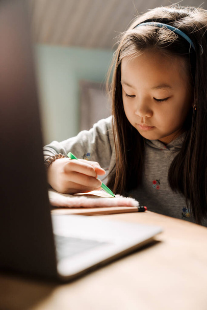 Asian girl doing homework with laptop while sitting at table at home - Valokuva, kuva