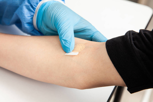 Krankenschwester legt einem Patienten nach der Entnahme einer Blutprobe ein Pflaster auf den Arm - Foto, Bild