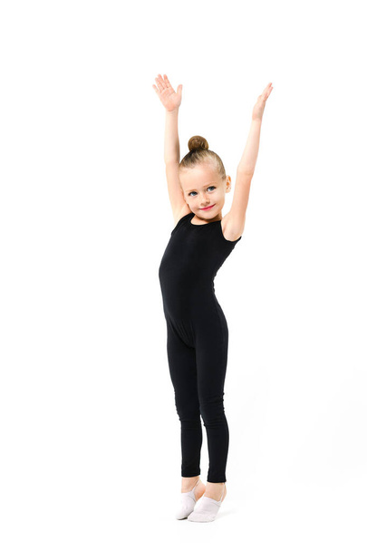 Lovely small gymnast acrobat dancer girl in black leotard with makeup full length stand on toes and raise hands up at isolated background - Photo, Image
