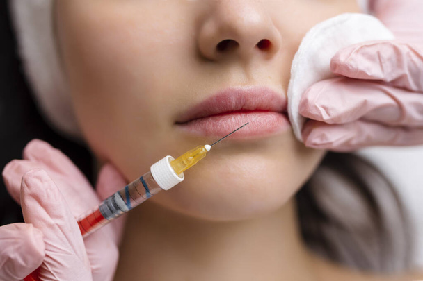 ajak alakú korrekciós eljárás kozmetikai szalonban. A szakorvos a beteg ajkán adja be az injekciót. Ajaknagyobbítás - Fotó, kép