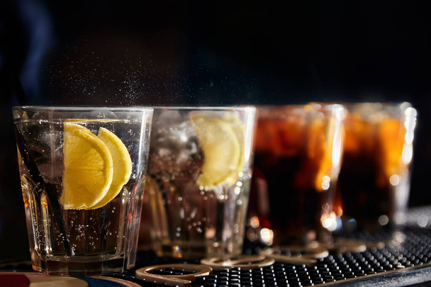Алкогольні коктейлі зі скибочками льоду та лимона на барі на темному фоні
 - Фото, зображення