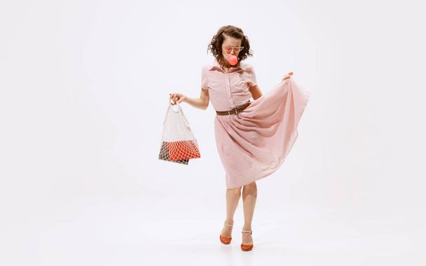 Portrait of beautiful woman eating bubblegum, posing with string bag isolated on white background. Daytime walk. Concept of beauty, retro style, fashion, elegance, 60s, 70s, family. Copy space for ad - Fotografie, Obrázek