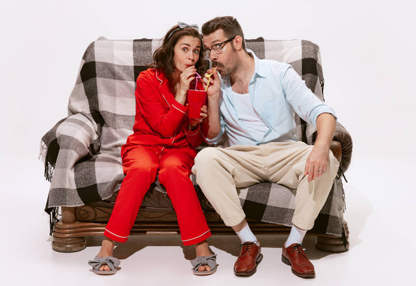 Portrait of couple, man and woman watching TV, movie together isolated on white background. Drinking from one cup. Concept of love, relationship, retro style, creativity, family. Copy space for ad - Photo, Image