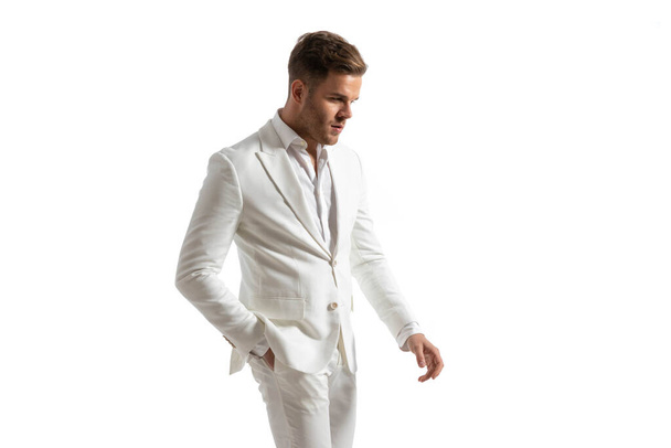 portret van vrolijke elegante man in wit pak houden hand in hand en op zoek naar kant in de voorkant van witte achtergrond in de studio - Foto, afbeelding