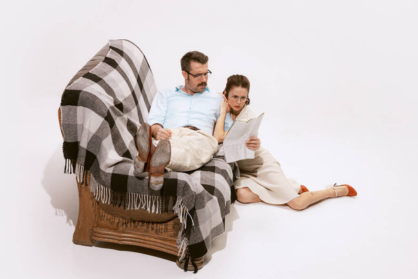 Portrait of beautiful couple, man and woman reading newspaper together isolated over white background. Concept of love, relationship, retro style, creativity, family. Copy space for ad - Фото, изображение