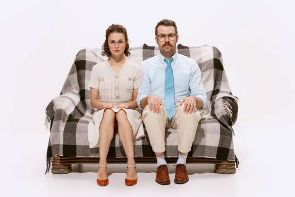 Porträt eines ernsten Mannes und einer ernsten Frau, die auf einem Sofa sitzen und isoliert vor weißem Hintergrund in die Kamera schauen. Konzept der Liebe, Beziehung, Retro-Stil, Kreativität, Familie. Kopierraum für Werbung - Foto, Bild