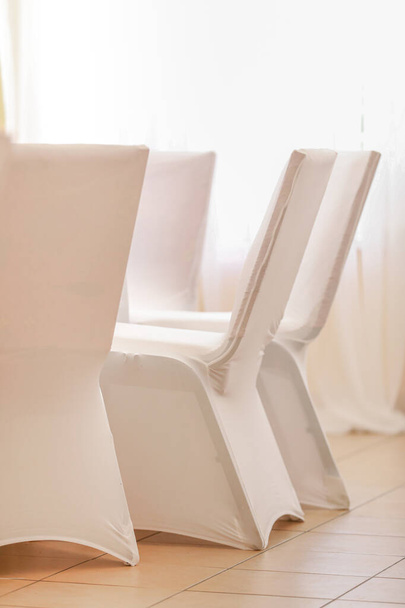 Καρέκλες συμποσίων καλυμμένες με λευκό ύφασμα τοποθετημένες στη σειρά κατά την προετοιμασία για την τελετή υποδοχής - Φωτογραφία, εικόνα
