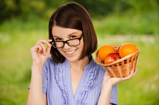 Молодая веселая женщина в очках держит корзину с фруктами
 - Фото, изображение