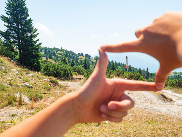 Garçon encadrant à la main signe touristique en bois à la route de gravier au sommet de la colline. Profitez du trek et du moment amusant. Alpes de Dolomite, région de Trente, Italie  - Photo, image