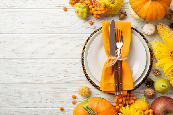 Thanksgiving day concept. Top view photo of plate knife fork napkin raw vegetables pumpkins maize pattypans apple pear walnut acorn pine cones rowan sunflowers isolated white wooden table background - 写真・画像