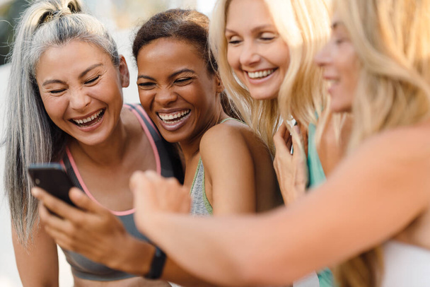 Multiracial women laughing and using cellphone during workout outdoors - Fotó, kép