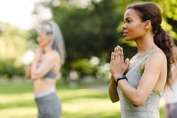 Multiracial women meditating during yoga practice in green park - Valokuva, kuva
