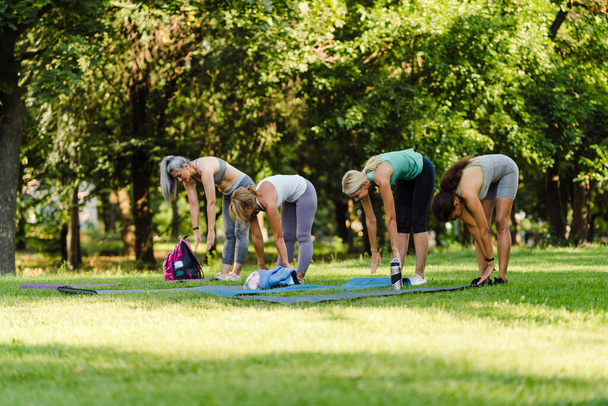 Multiracial women doing exercise during yoga practice in summer park - 写真・画像