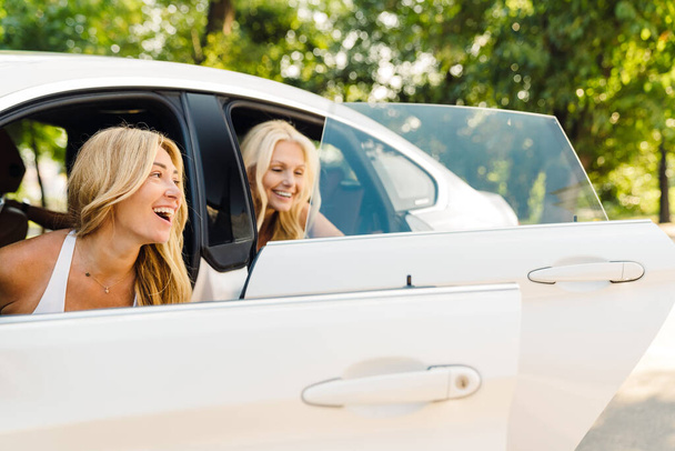 White women smiling while getting out of car in summer park - Fotó, kép