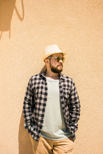 Young fashion elegant stylish man posing on streets of european city. Bearded handsome hipster man posing near wall with hard shadows on hot noonday - summer vacations and holiday - Foto, afbeelding