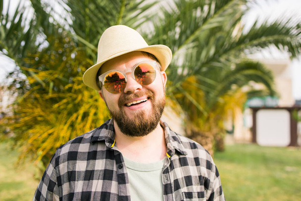 Rindo homem atraente usando chapéu sobre palmeira fundo emoção e férias de viagem - Foto, Imagem