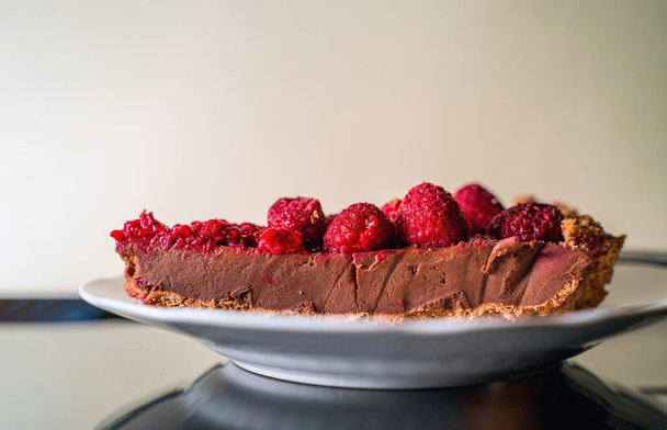 Un trozo de una deliciosa tarta de chocolate con frambuesa en el plato blanco sobre fondo blanco, primer plano de postre de pastel de frutas - Foto, Imagen