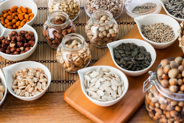 Rustic wood table filled with a large assortment of nuts like pistachios, hazelnut, pine nut, almonds, pumpkin seeds, sunflower seeds, peanuts, cashew and walnuts - Photo, image