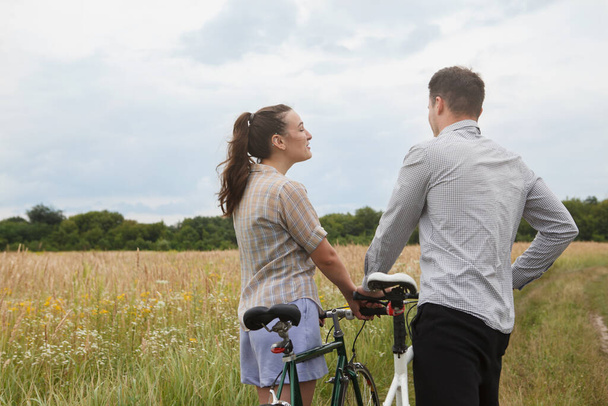 The happy couple cycling near the field. Cyclists man and a woman with bicycles go near the fields  in summer. - Fotó, kép