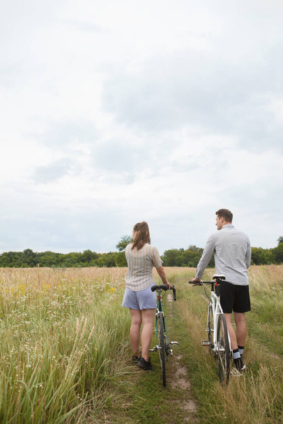 Het gelukkige paar fietsen in de buurt van het veld. Fietsers man en een vrouw met fietsen komen in de zomer in de buurt van de velden. - Foto, afbeelding