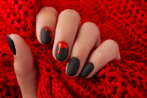Feche a mão de mulheres com a manicura de Halloween no fundo vermelho que mantém o tecido. Manicure, conceito de salão de beleza pedicure. Design de unhas na moda - Foto, Imagem