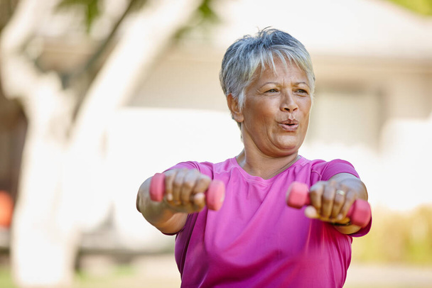 Staying strong in her senior years. a mature woman lifting dumbbells outside - Foto, immagini