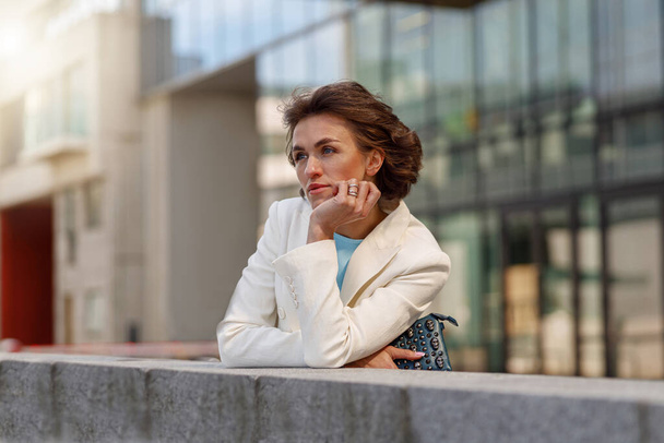 Окаменелая женщина в белом костюме стоит возле бизнес-центра и смотрит в сторону - Фото, изображение