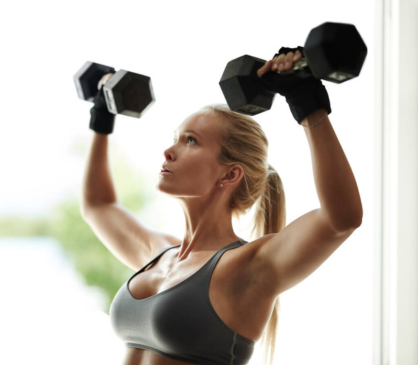 If it doesnt burn, youre not doing it right. a beautiful young woman in workout gear lifting dumbbells - Valokuva, kuva