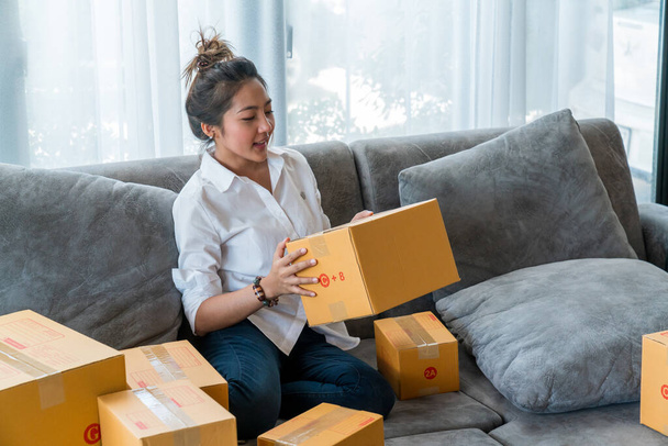 Kanepede oturan güzel Asyalı kadınlar küçük işletmelerle dolu bir sürü paket kutusuyla online alışveriş yapan müşterilere satıyorlar. İnternet üzerinden satış ve alışveriş kavramı - Fotoğraf, Görsel