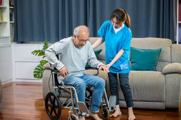 Asian nurse assisting helping senior man patient get up from wheelchair for practice walking at home, Smiling doctor support old man to getting up, help handicapped elderly stand up, healthcare - Foto, imagen
