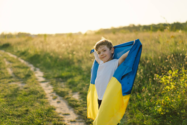 Ukraines Independence Day. Ukrainian child boy in white t shirt with yellow and blue flag of Ukraine in field. Flag of Ukraine. Constitution day. Stand with Ukraine and Save - Zdjęcie, obraz