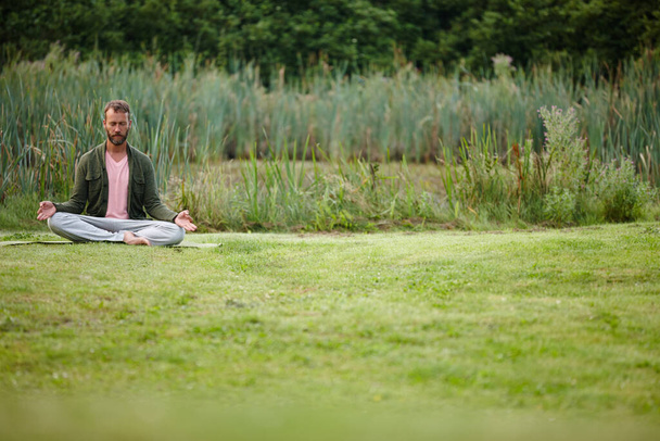 Stając się jednością z naturą. przystojny Dojrzały mężczyzna medytujący w pozycji lotosu w naturze - Zdjęcie, obraz