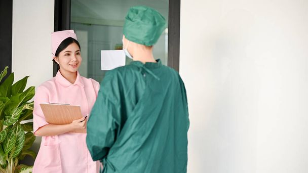 Attraktive junge asiatische Krankenschwester im Gespräch mit einer Chirurgin vor dem Operationssaal. Arzt, Arzt, Chirurg - Foto, Bild