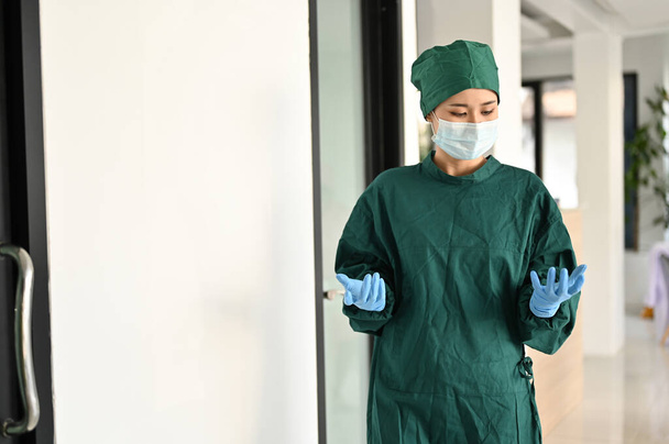 Professional Asian female doctor or surgeon in green surgical gown and medical mask walking along the operating room. Health care and surgery concept - Foto, Imagen