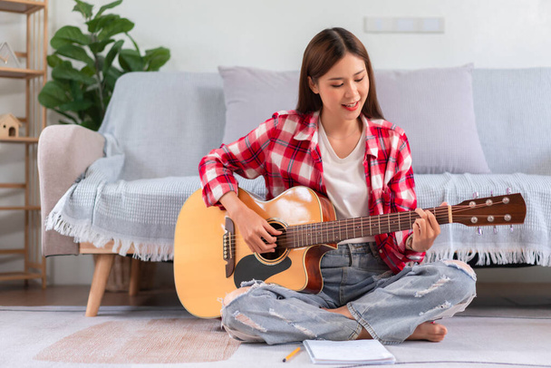 Hobbi koncepció, fiatal ázsiai nő ül a padlón játszani akusztikus gitár után komponált új dalt. - Fotó, kép