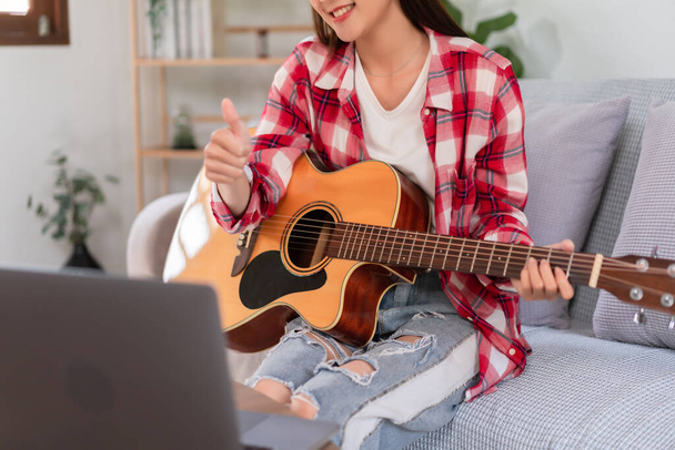 концепція хобі, молода азіатка грає на акустичній гітарі в прямому ефірі і робить великі пальці вгору жест
. - Фото, зображення
