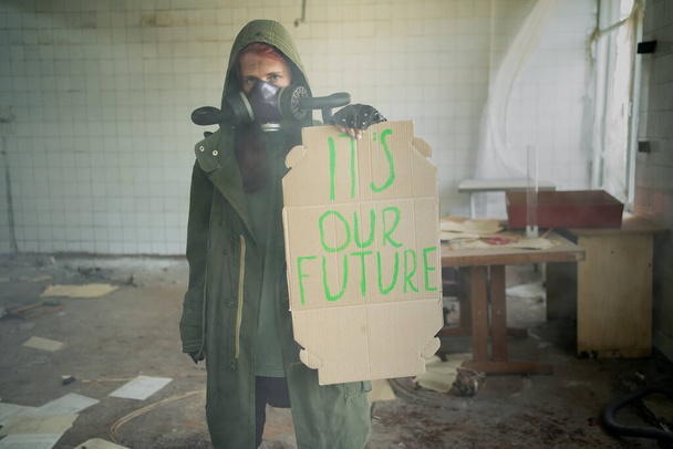 Zanieczyszczenie środowiska, katastrofa ekologiczna, wojna nuklearna, kobieta w masce gazowej z transparentem, który mówi: to nasza przyszłość. Koncepcja apokalipsy. osłona twarzy zapobiegająca wdychaniu toksycznego powietrza. - Zdjęcie, obraz
