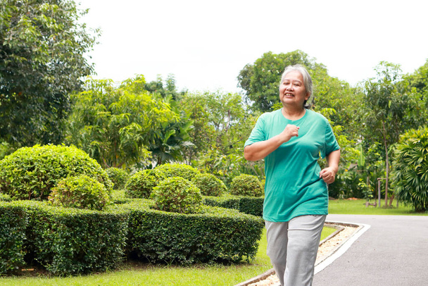 starsza kobieta Uśmiechnij się i ciesz ćwiczeniami. Starsi biegają w parku. Pojęcie opieki zdrowotnej jako zdrowej na emeryturze - Zdjęcie, obraz