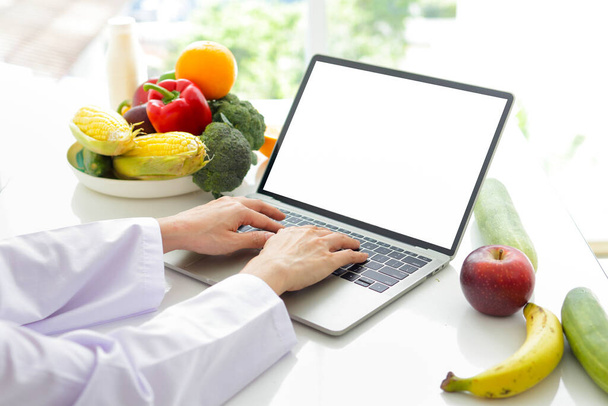Aziatische vrouwelijke arts of voedingsdeskundige Gebruik een laptop voor online videogesprekken. Geef de patiënt advies over eten. online patiënt gezondheidszorg concept Gezond eten. Afvallen. wit scherm. - Foto, afbeelding