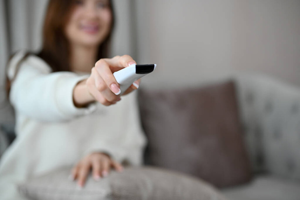 Attractive and happy young woman in the living room watching TV and holding a TV remote control. cropped and selective focus image - 写真・画像