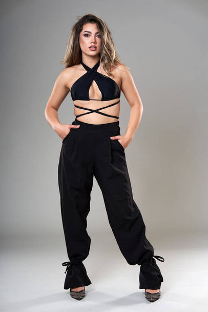 Young beautiful fashionable model in trendy black top and trousers studio shot on gray background - Foto, imagen