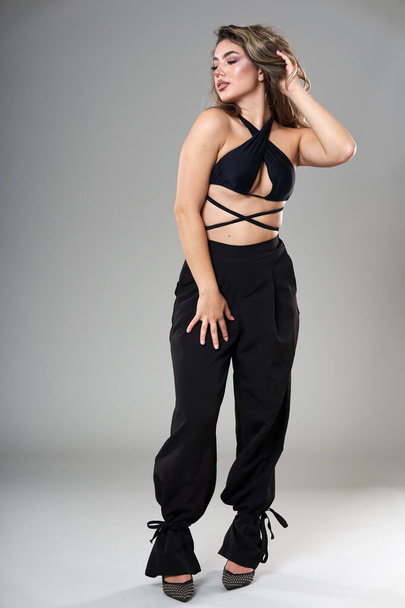 Young beautiful fashionable model in trendy black top and trousers studio shot on gray background - Foto, afbeelding