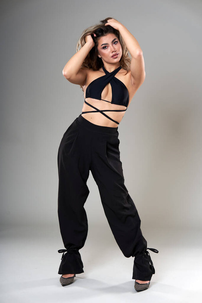 Young beautiful fashionable model in trendy black top and trousers studio shot on gray background - Фото, изображение
